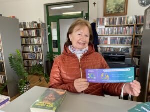Czytelniczka prezentująca bilet udziału w akcji z biblioteką dookoła świata