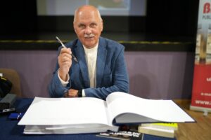 Spotkanie Dobry klimat - Tomasz Zubilewicz z długopisem w ręku, przed nim kronika biblioteki