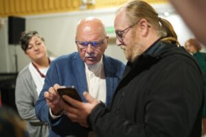 Spotkanie Dobry klimat - pan Tomasz i mężczyzna- uczestnik spotkania wpatrzeni w telefon i omawiający wyświetlony obraz