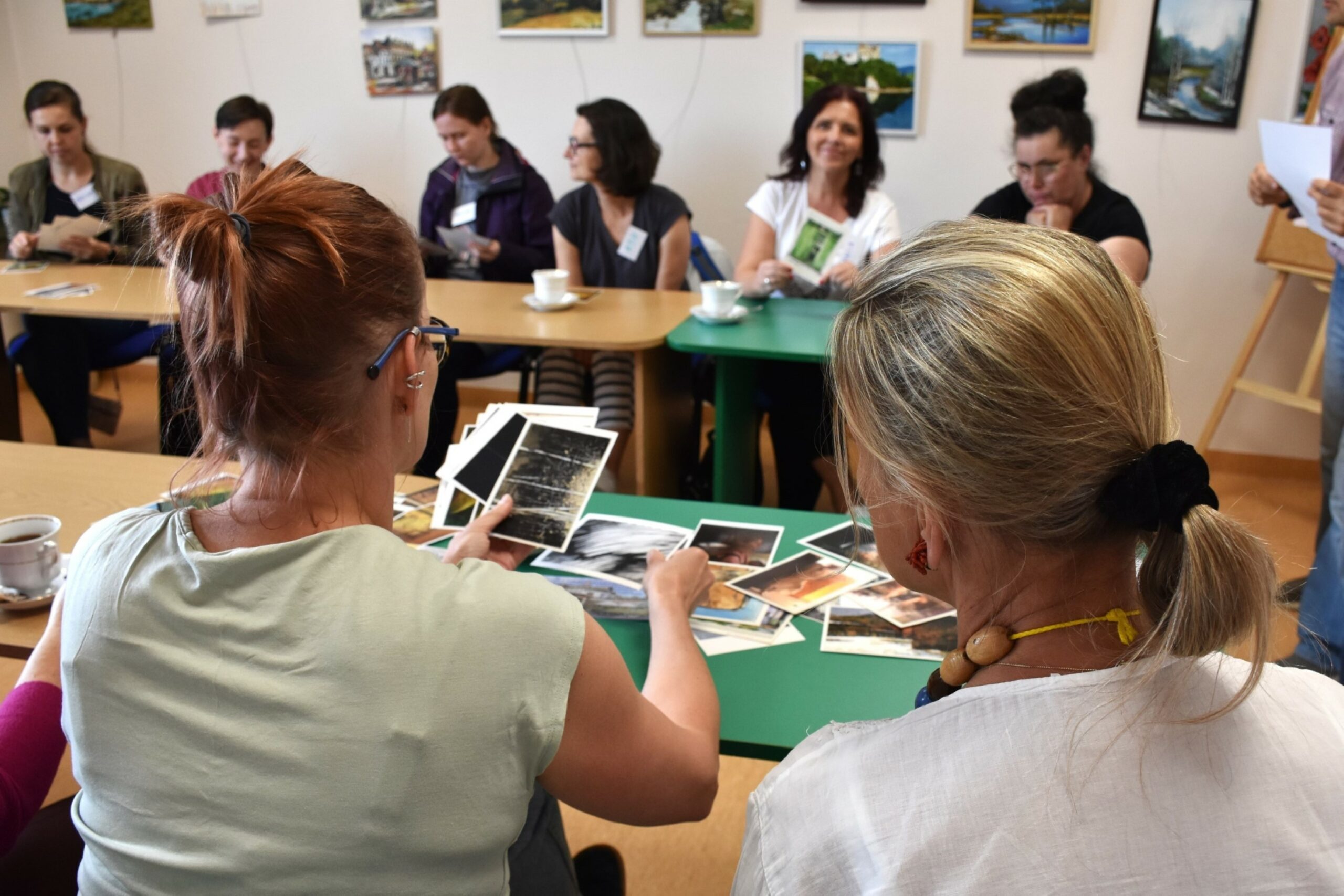 Dwie uczestniczki warsztatu paleta emocji tyłem, na pierwszym planie pocztówki z reprodukcjami obrazów