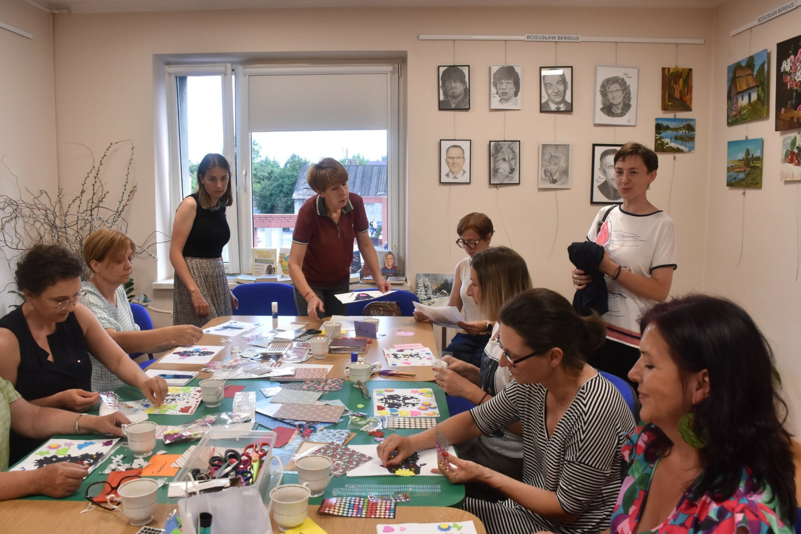 Dziewięć uczestniczek warsztatu oswoić lęk przy stole pełnym materiałów papierniczych pracuje nad swoimi obrazkami