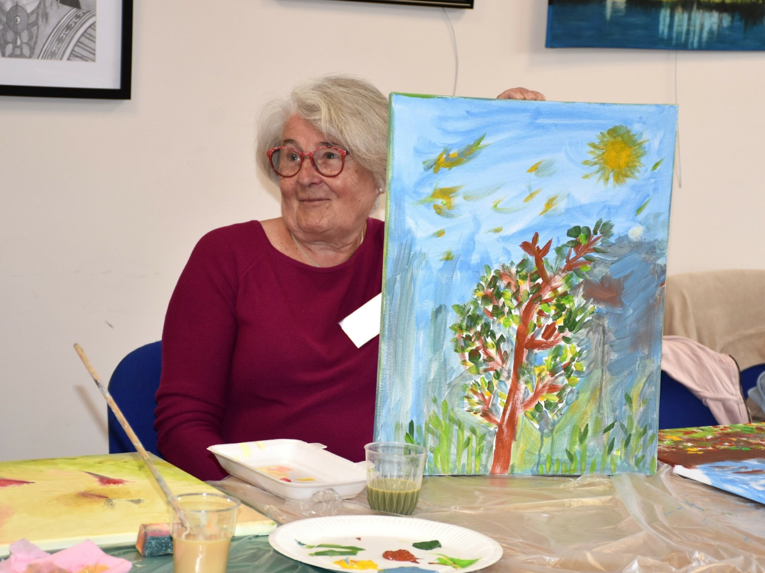 Seniorka uczestnicząca w warsztacie paleta emocji pokazująca namalowany przez siebie obraz na płótnie
