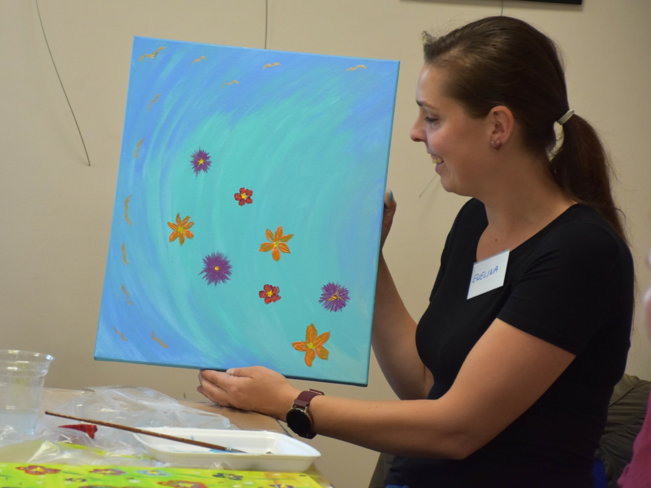 Uczestniczka warsztatu paleta emocji prezentująca obraz malowany na płótnie - małe kwiaty na niebieskim tle