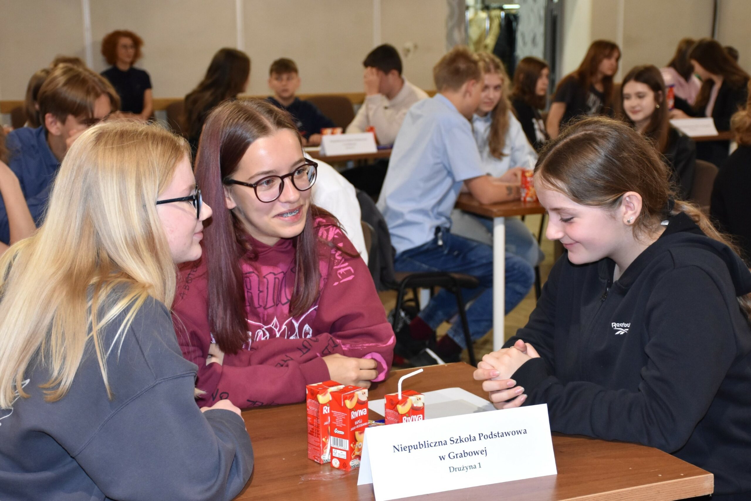 Uczestniczki turnieju wiedzy o książce i bibliotece - trzy nastolatki w uśmiechu siedzące przy stoliku