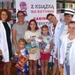 Mama, trójka dzieci i cztery bibliotekarki w lekarskich kitlach, z książkami w ręku, w tle baner akcji Literatura na receptę