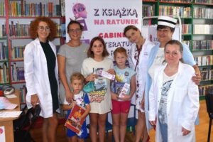 Mama, trójka dzieci i cztery bibliotekarki w lekarskich kitlach, z książkami w ręku, w tle baner akcji Literatura na receptę