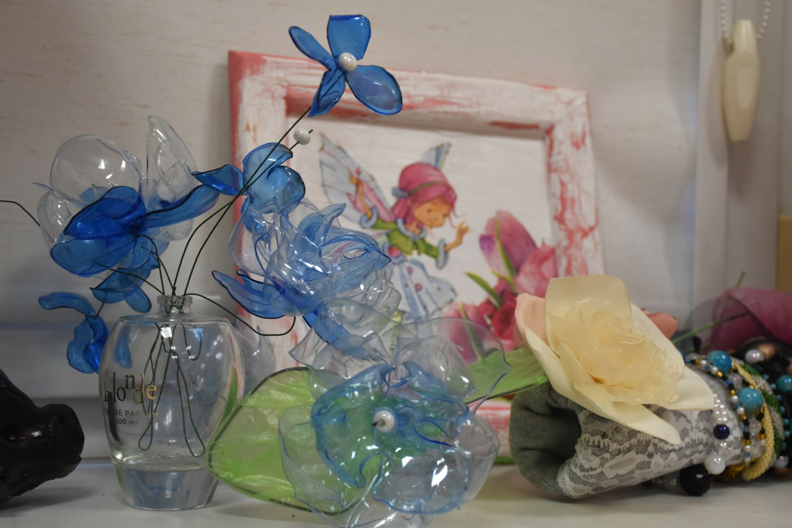 Zdjęcie niebieskich kwiatów topionych z plastiku, w tle obrazek wróżki wykonany metodą decoupage