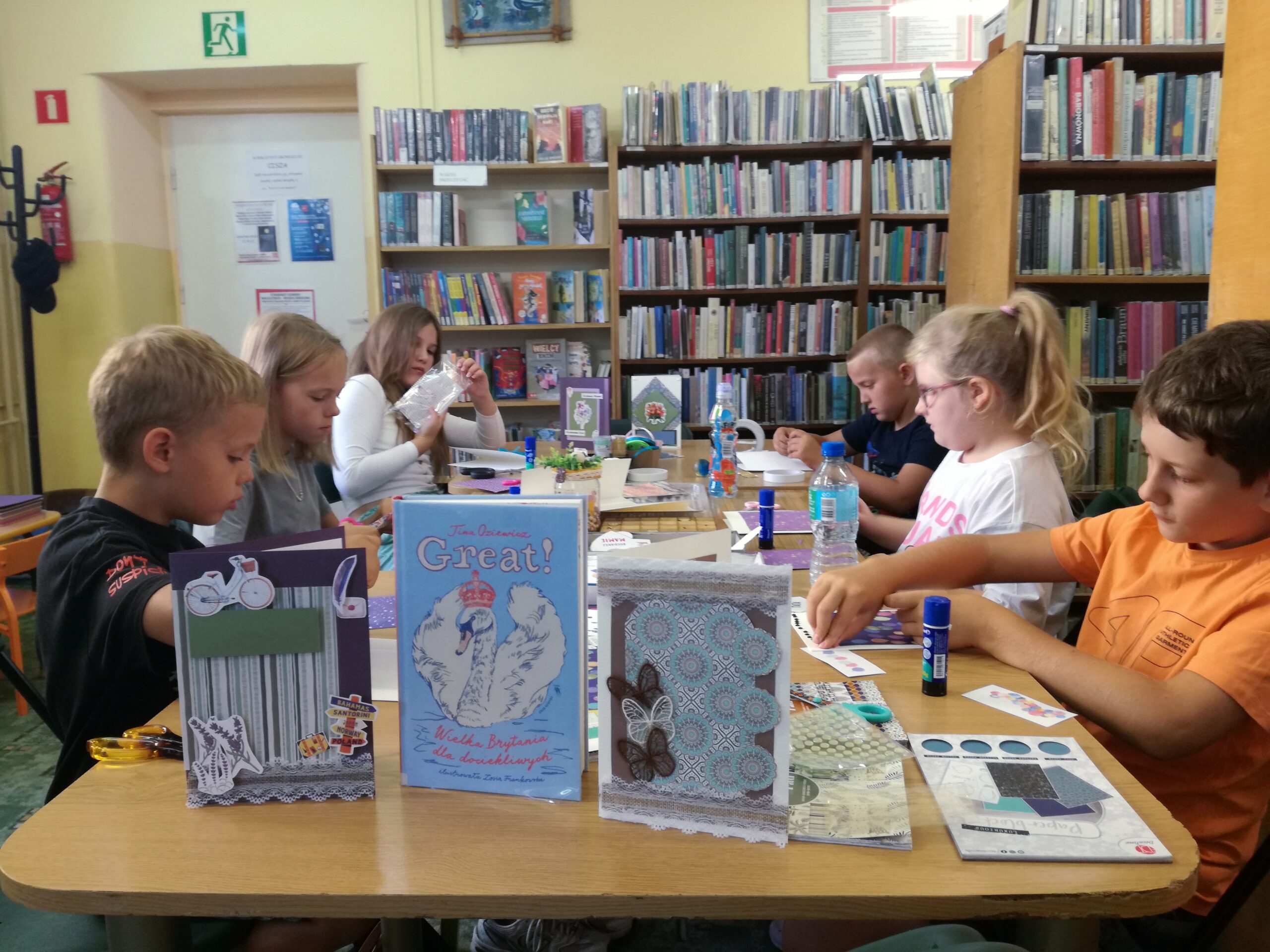 Dzieci przy stole tworzące ozdobne kartki z różnych papierów z wakacji