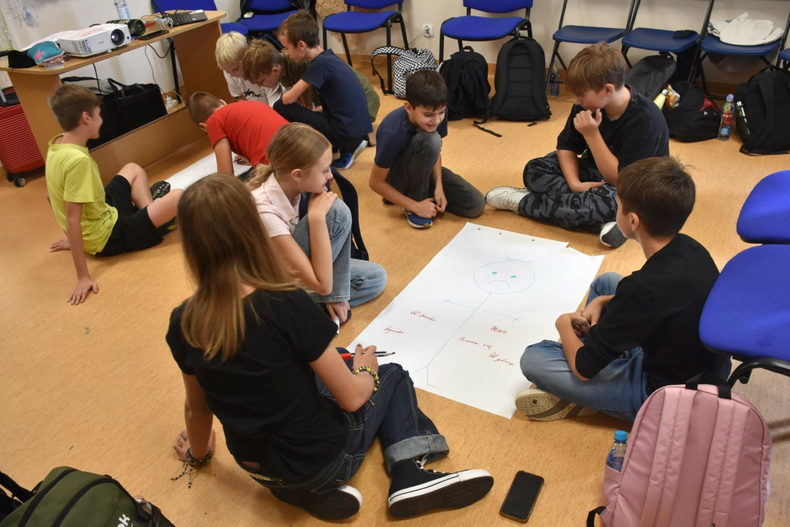 Dziesięciu nastolatków siedzących na podłodze wokół dwóch dużych arkuszy białego papieru