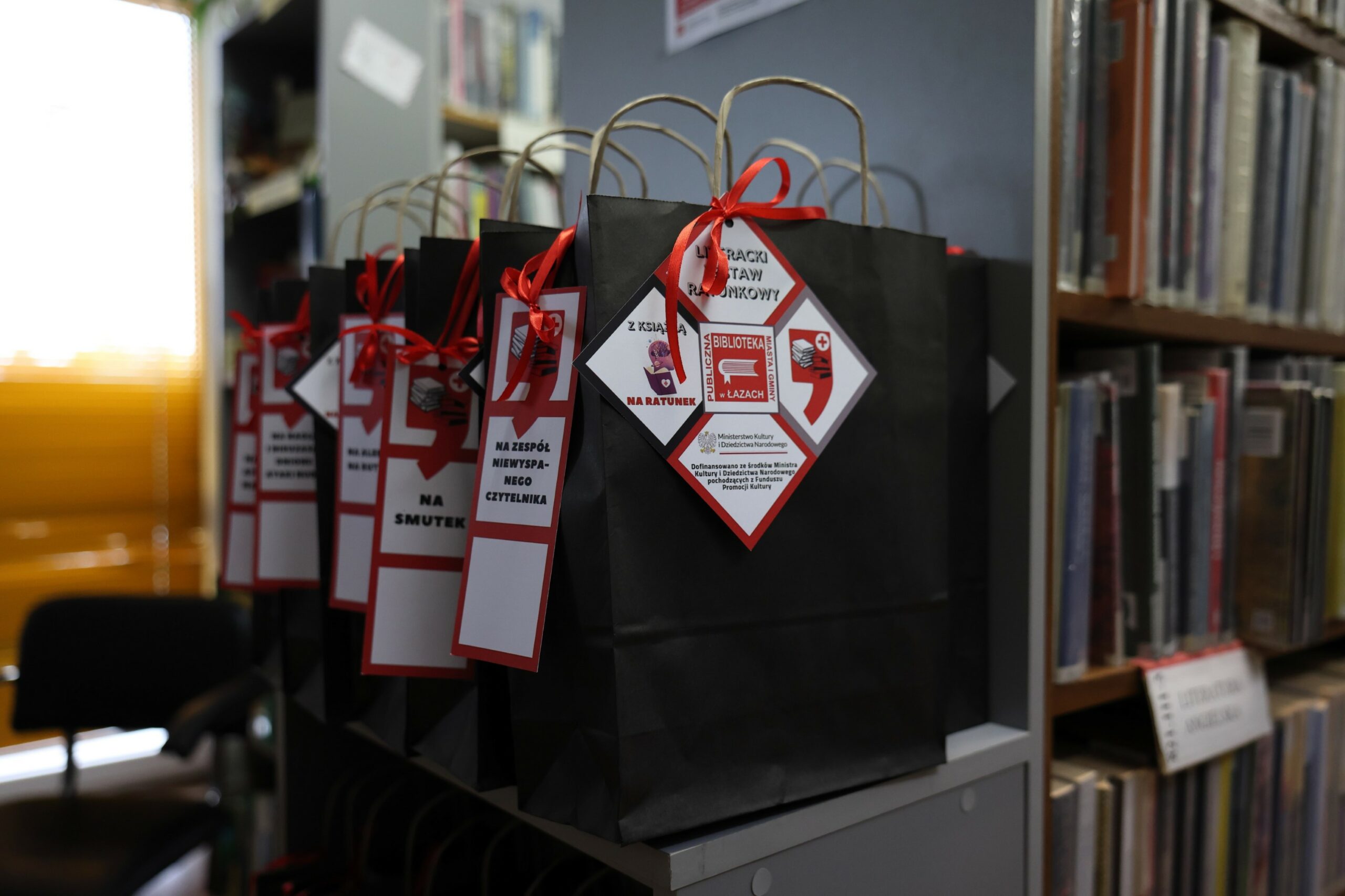 Czytelniczka, bibliotekarka, stos książek i czarna papierowa torba z logiem akcji literacki Zestaw ratunkowy - Zdjęcie portretowe