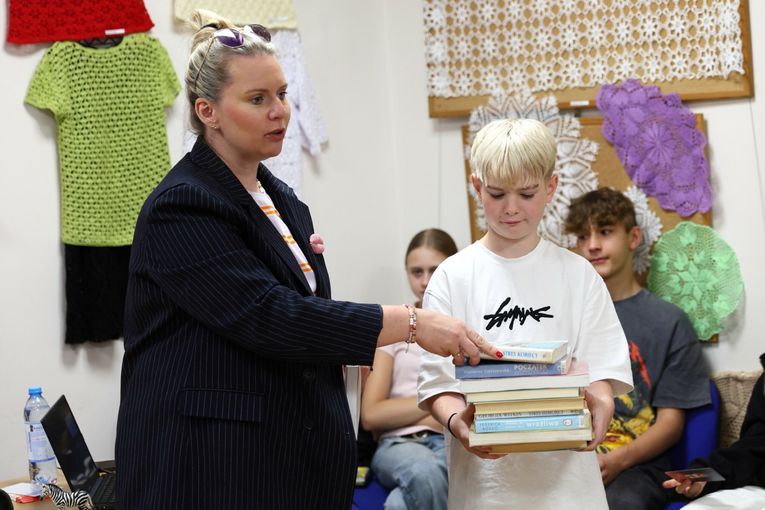 kobieta z kokiem kładąca szóstą książkę na stosie książek trzymanym przez nastoletniego chłopca