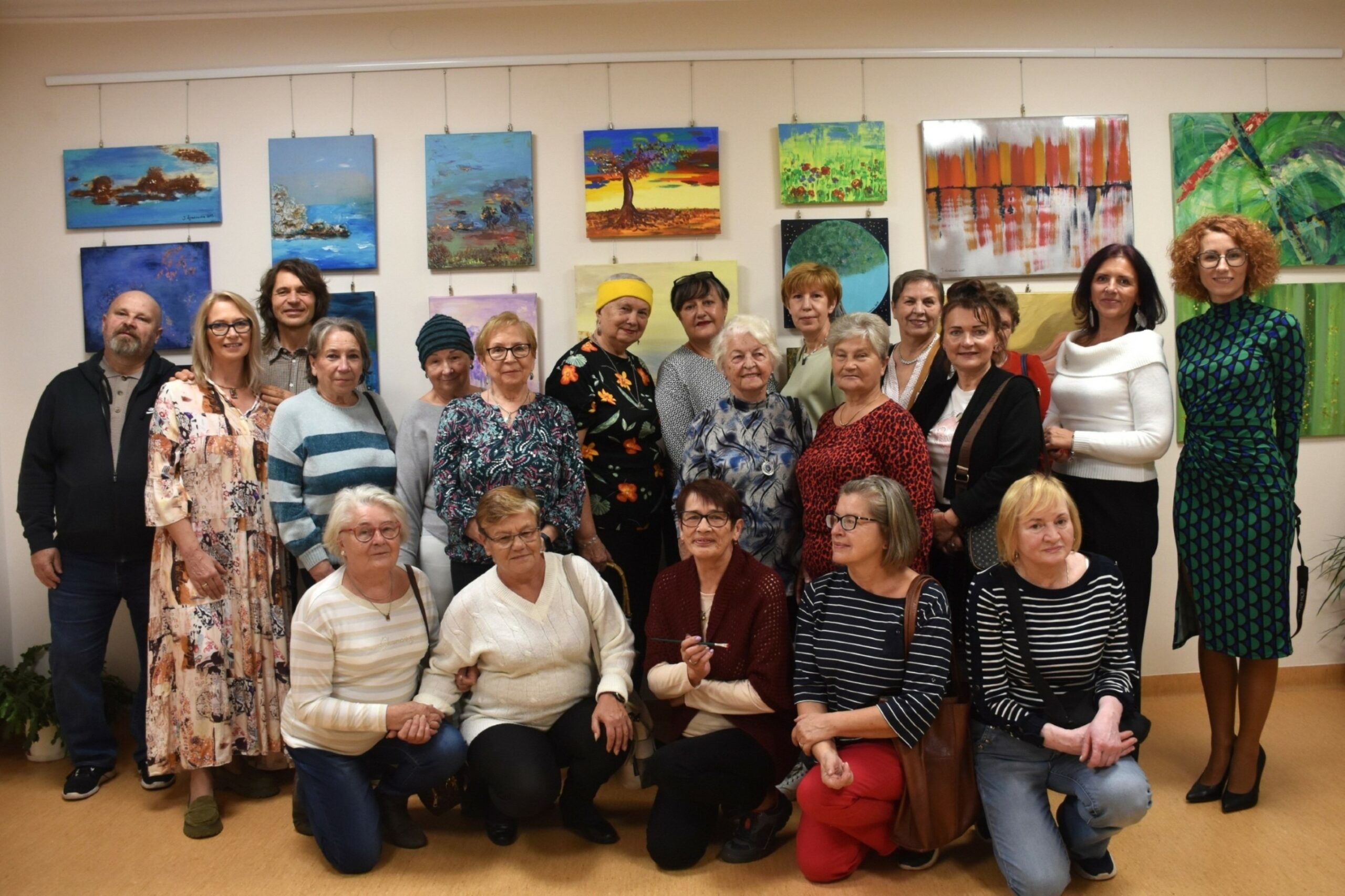 Zdjęcie grupowe uczestników wernisażu wystawy sztuka dnia codziennego, w tle obrazy Jolanty Łysakowskiej