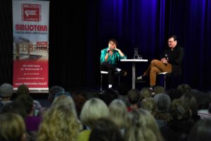 Autorka i moderator siedzący na scenie, widok z oddali, fotografia Jerzy Kleszcz