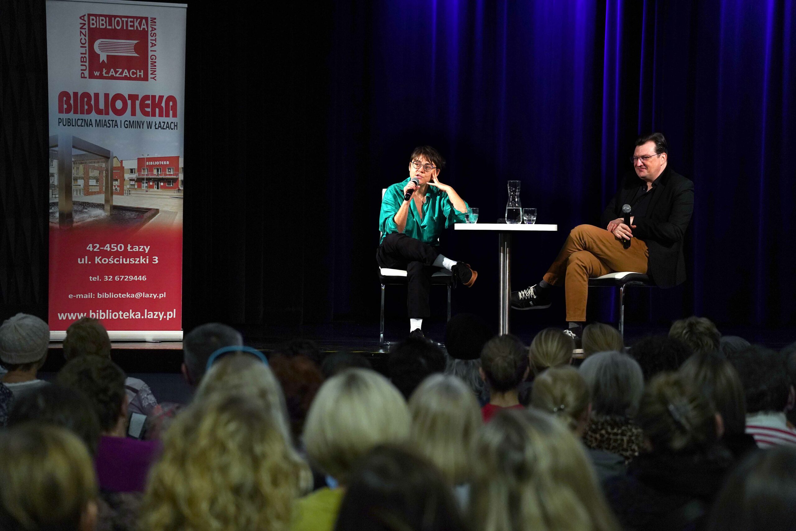 Autorka i moderator siedzący na scenie, widok z oddali, fotografia Jerzy Kleszcz