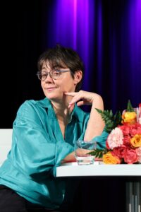 Autorka oparta łokciem o stolik, pozująca do zdjęcia z zawiadiackim spojrzeniem