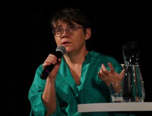 Autorka z mikrofonem w ręku i uniesioną ręką, wpatrująca się w dal fotografia Jerzy Kleszcz