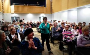 Autorka idąca przez salę pełną siedzących ludzi fotografia Jerzy Kleszcz