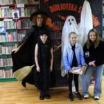 Duch i czarownica pozujące z trójką dzieci na tle regałów