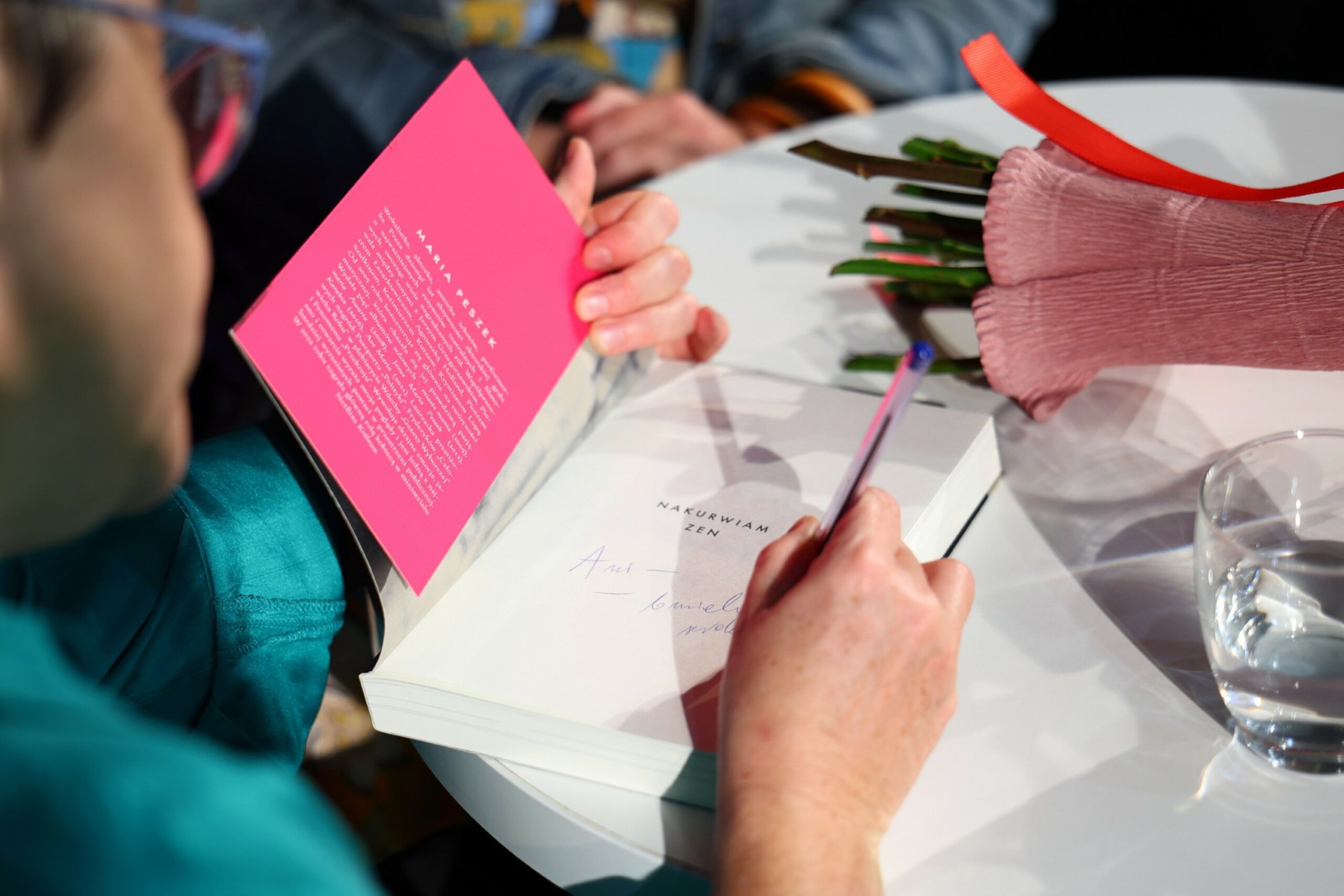 Widok otwartej książki i ręki autorki z długopisem dokonującej wpisu