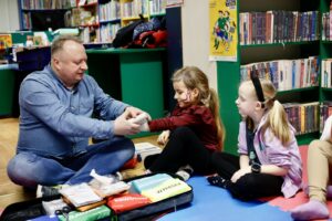 Doktor bandażujący nadgarstek dziewczynki i przyglądająca się tej sytuacji, wszyscy siedzą na macie, na podłodze