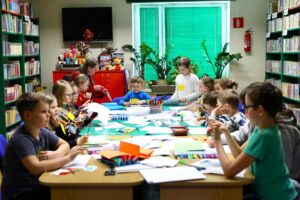 Widok dzieci wycinających przy stole wypełnionym materiałami papierniczymi