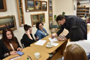 Prowadzący szkolenie pochylony nad kartką papieru, piszący kod dla grupy pięciu uczestniczek szkolenia