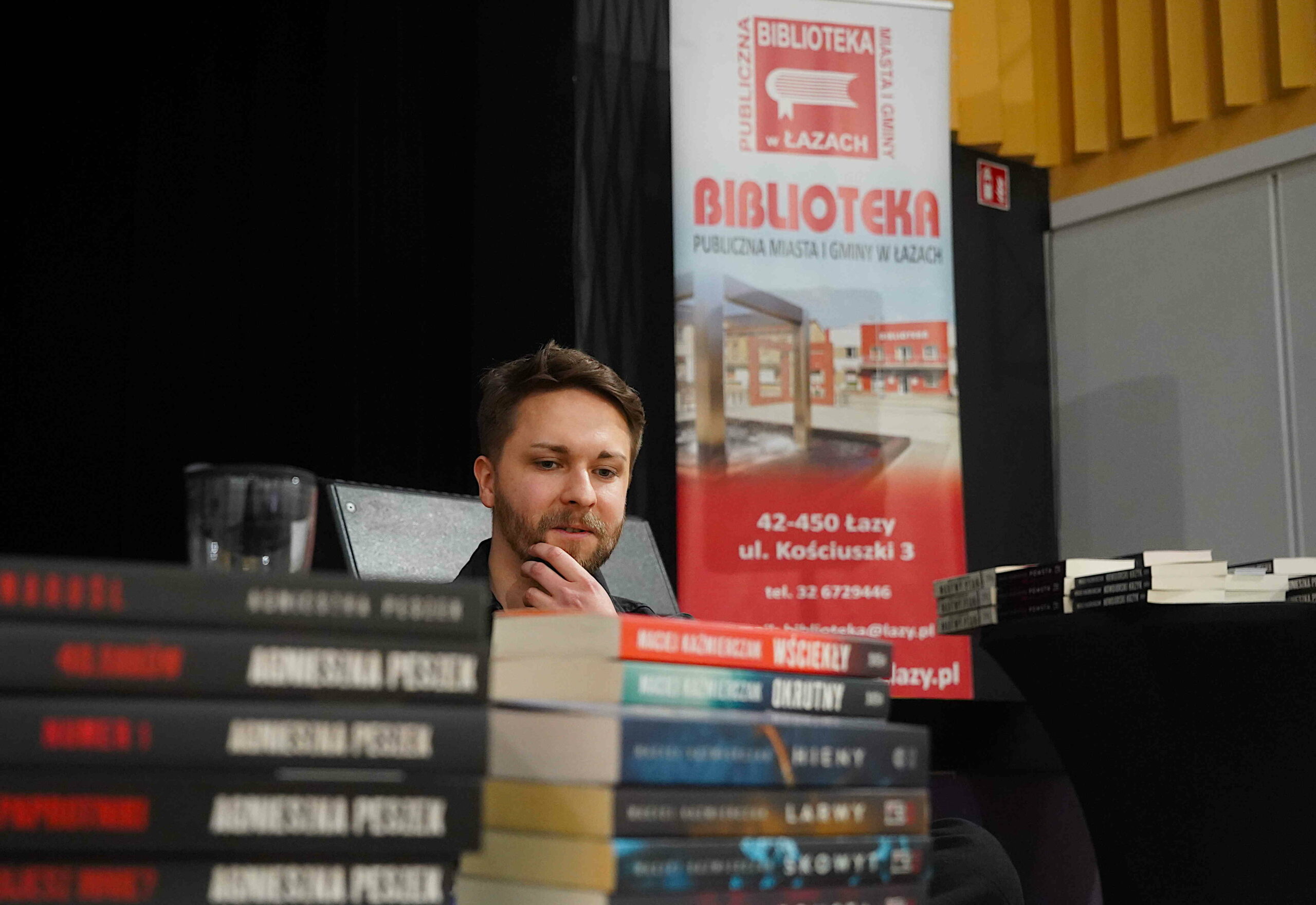 Twarz autora w zamyśleniu, na pierwszym planie stosy książek