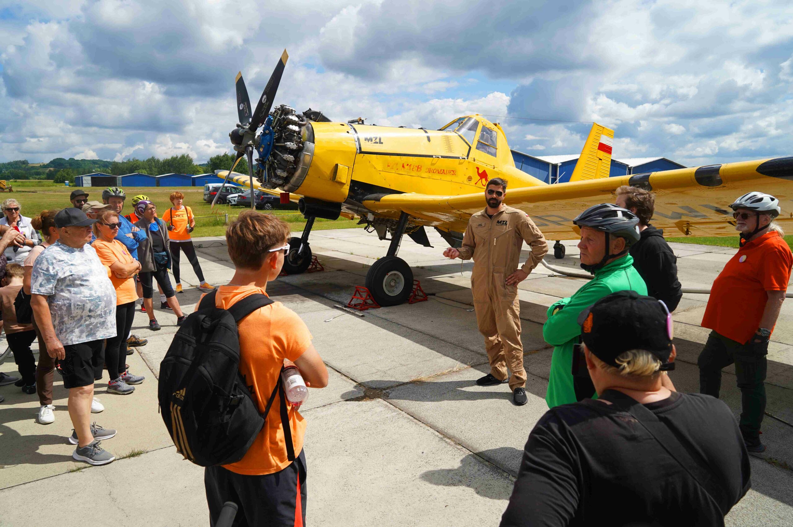 Pilot stojący przy żółym samolocie dromader otoczony kilkoma ludźmi