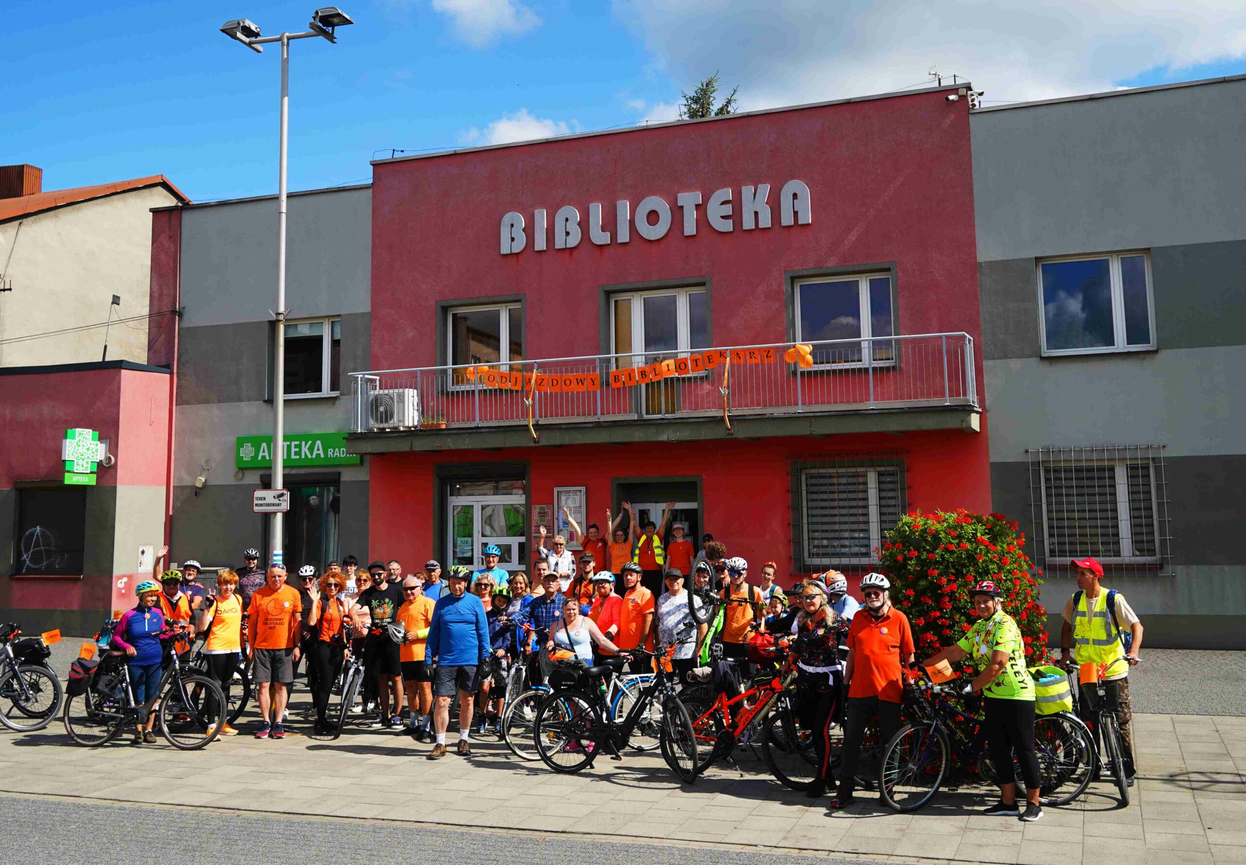 Zdjęcie grupowe uczestników przejazdu rowerowego Odjazdowy Bibliotekarz, w tle Biblioteka w Łazach