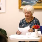 Autorka Maria siedząca przy stoliku i czytająca tekst swojego wiersza