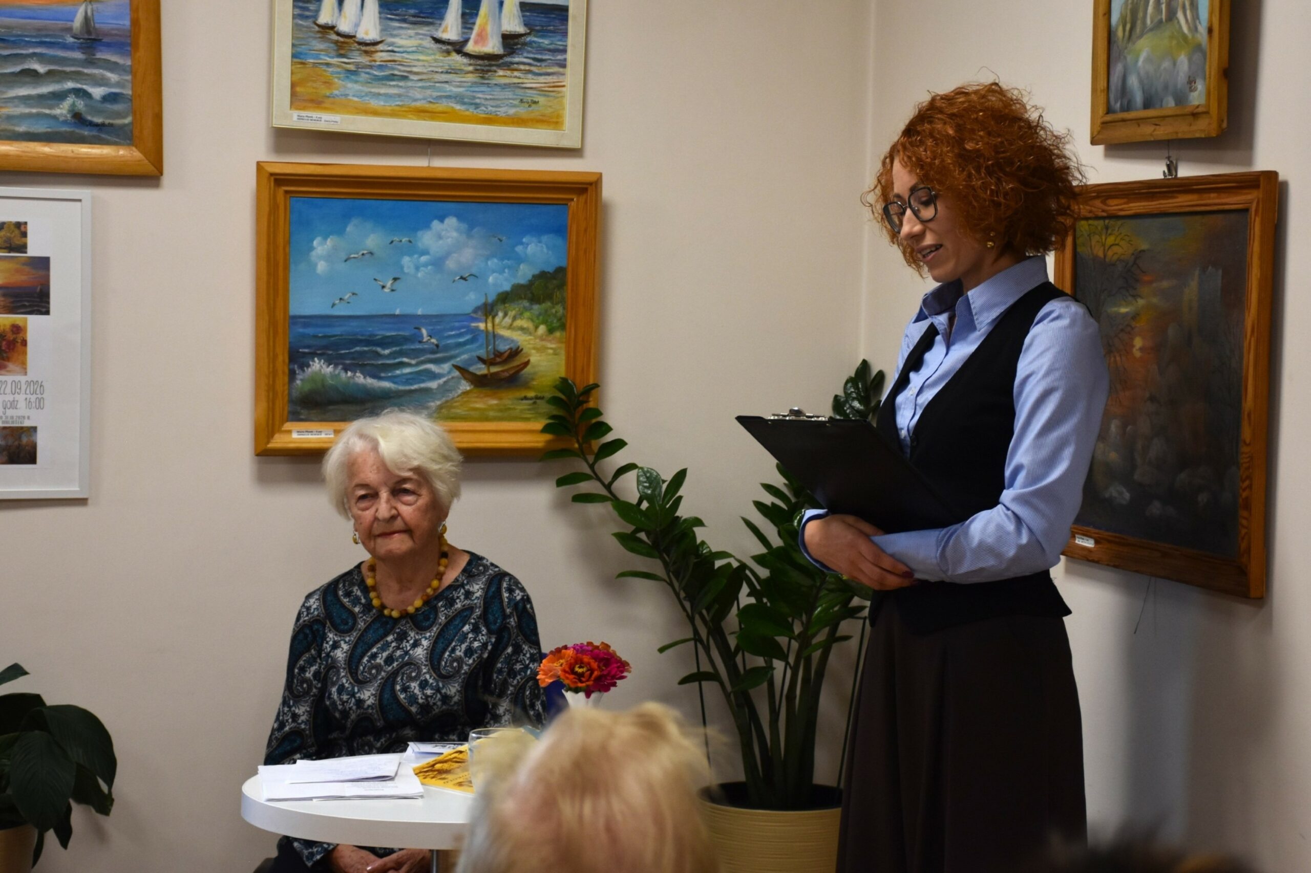 Dyrektor Biblioteki w Łazach mówiący o autorce Marii Płatek, na drugim planie siedząca autorka