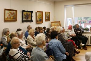 Uczestnicy wernisażu wystawy Między światłem a słowem siedzący na krzesłach w czytelni