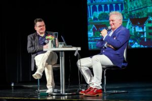 Autor i dziennikarz prowadzący spotkanie Granice świata siedzący przy stoliku na scenie miejskiego ośrodka kultury