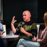 Marcin Margielewski mówiący do mikrofonu, z prawej i lewej strony bibliotekarki